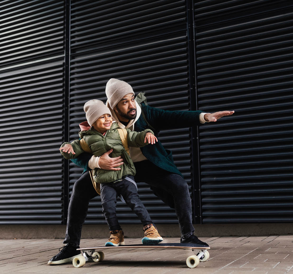 Father teaching his son skateboarding outdoor in a city.