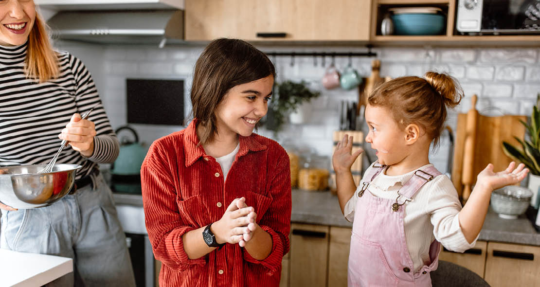 Mother with two daughters and a dog in the kitchen making pancakes.